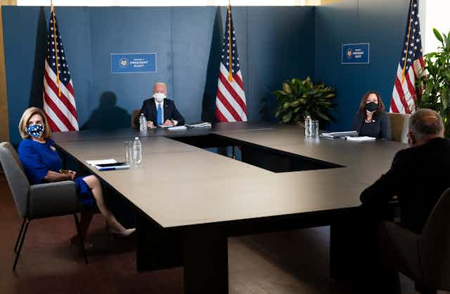 Joe Biden, Kamala Harris, Chuck Schumer and Nancy Pelosi sit far apart at a table. 