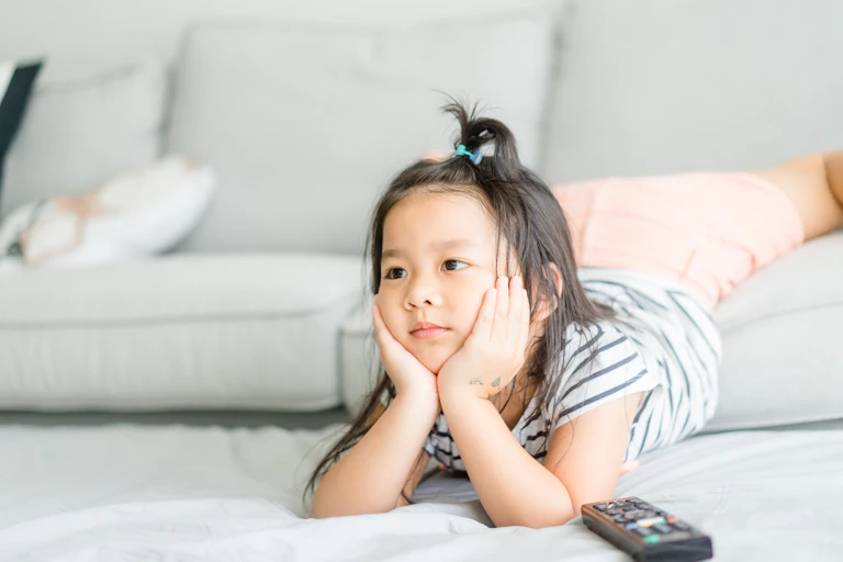 A young girl watches television with a remote on the ground next to her
