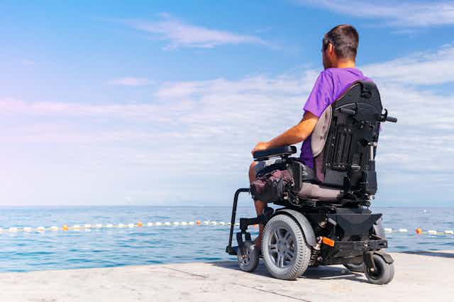 Un hombre en silla de ruedas eléctrica mira el mar.