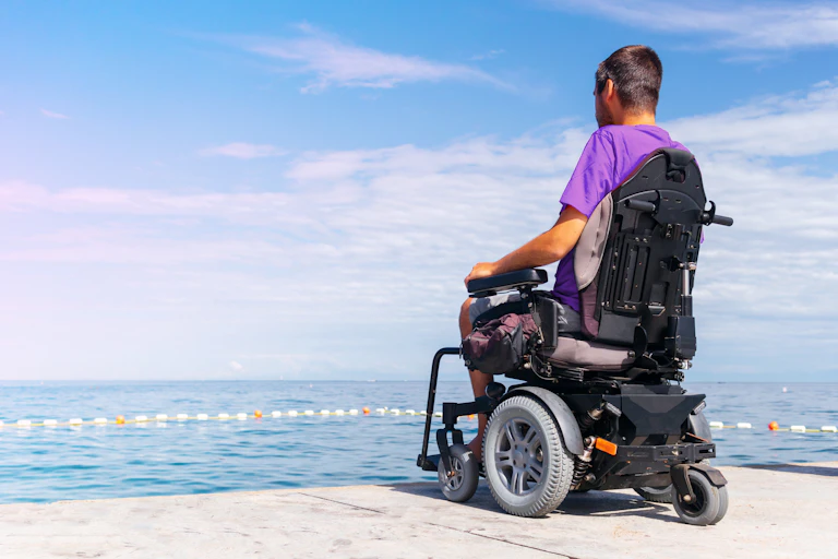 Un hombre en silla de ruedas eléctrica mira el mar.