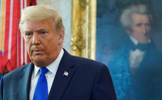 Donald Trump stands in front of a painting of Andrew Jackson in the Oval Office.