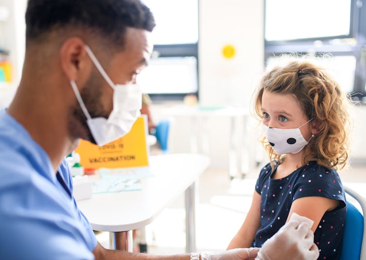 A doctor gives a young girl in a mask a vaccination.