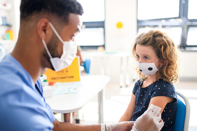 A child in a face mask gets vaccinated by a health-care worker in a face mask