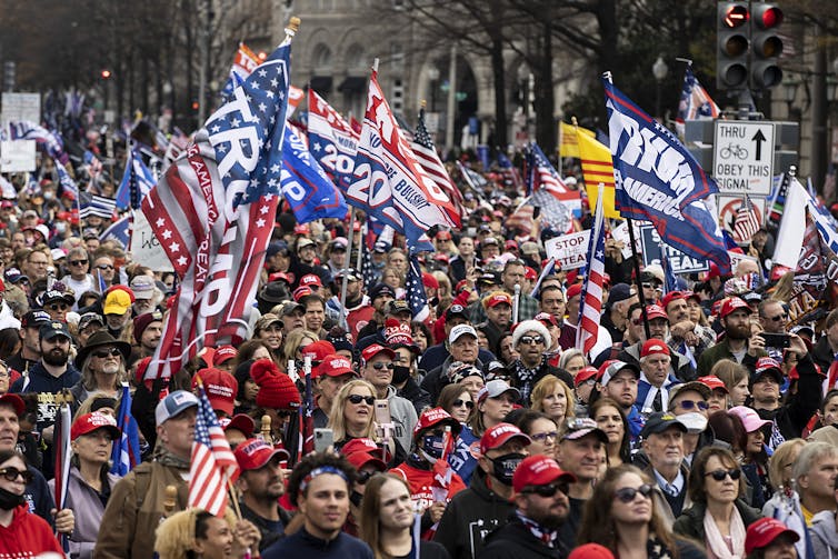 A crowd of Trump supporters wave Trump flags and wear red hats.