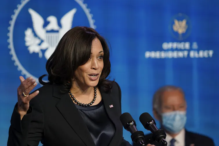 Kamala Harris delivers a speech. Joe Biden is sitting in the background.