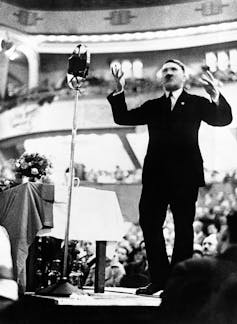 Adolf Hitler, dressed in a business suit, giving a speech.