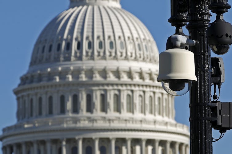 A security camera mounted on a streetlight pole with the U.S. Capitol dome in the background