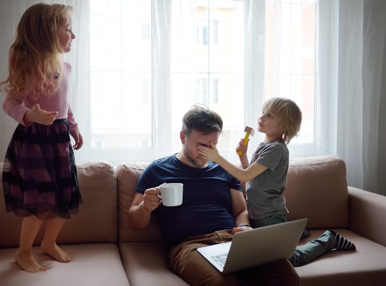 Dad trying to work on couch with kids jumping over him.