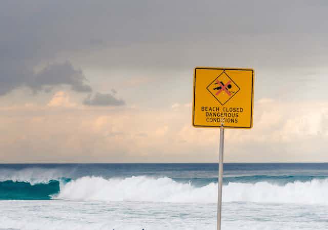 A beach sign reads: beach closed. Dangerous conditions.