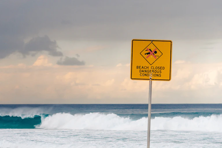 A beach sign reads: beach closed. Dangerous conditions.