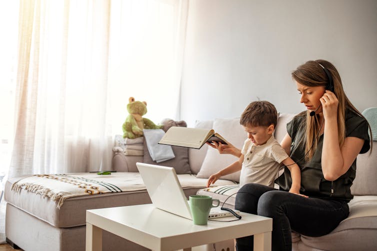 Woman struggling to work on her laptop with her toddler beside her.