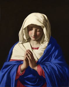 A painting of a woman in a vivid blue robe and white hood, with bowed head and clasped hands.