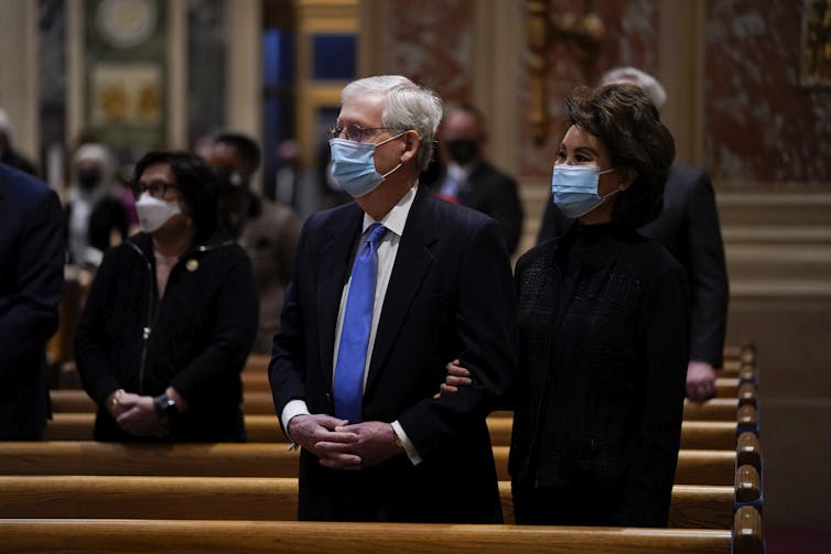 Senate Minority Leader Mitch McConnell and his wife Elaine Chao, in masks, stand behind a church pew.