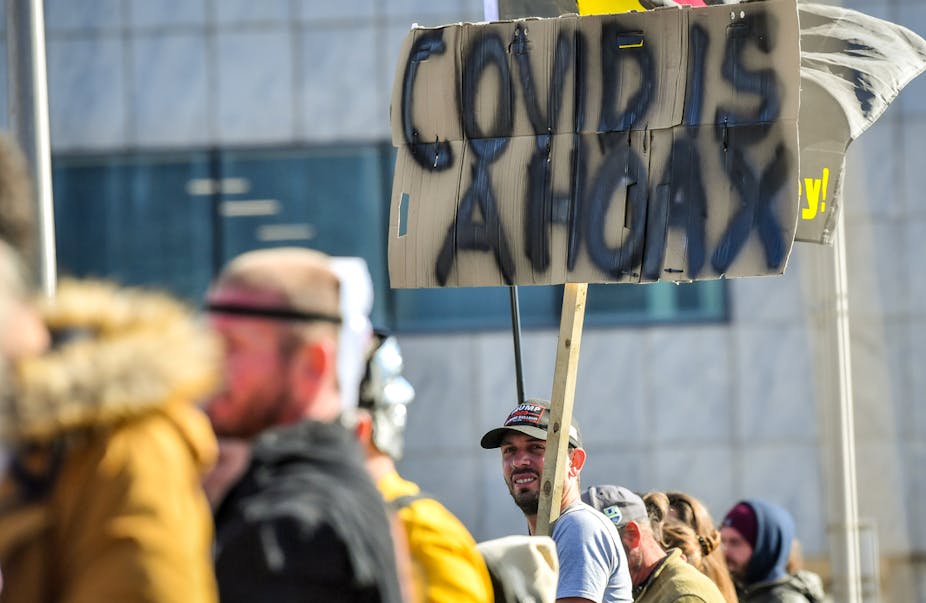 Man holding a sign reading 'Covid is a hoax'.