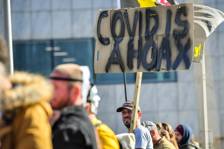 Man holding a sign reading 'Covid is a hoax'.