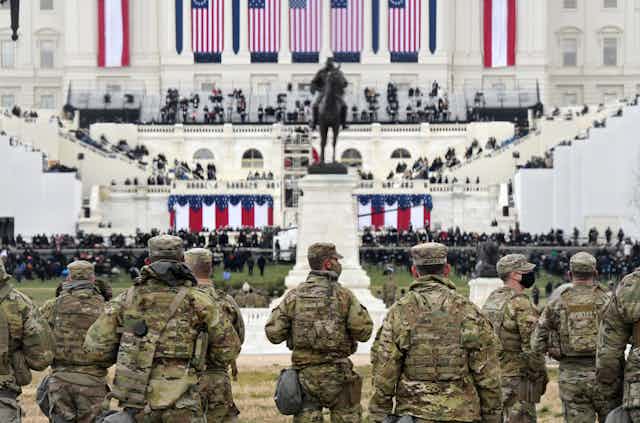 Members of the National Guard gather near the U.S. Capitol, with Biden's inaugural preparations visible in background