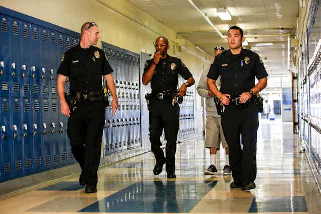 Three police officers walk down a school hallway. 