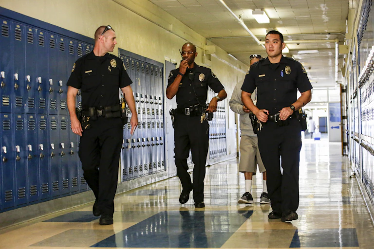Three police officers walk down a school hallway.