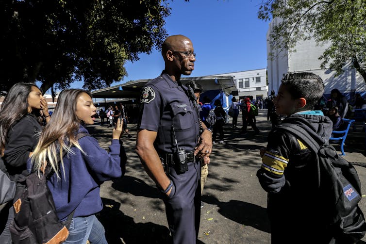 A police officer interacts with students on a schoolyard.