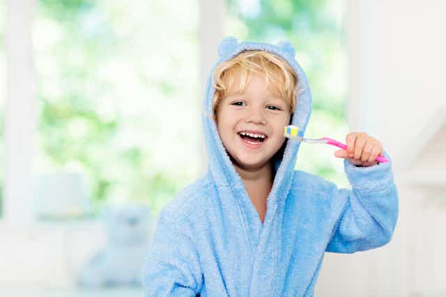 A young boy in his dressing gown smiling and holding a toothbrush.