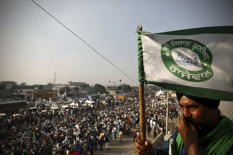 A man carries a flag. Behind him a crowd of protesters march along a road.