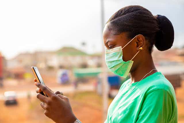 A surgical in a green surgical mask holding a mobile phone