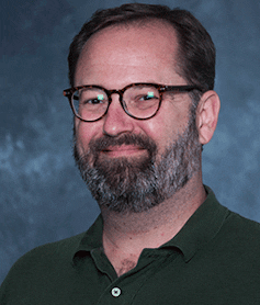 A photo of a man in a black shirt wearing glasses.