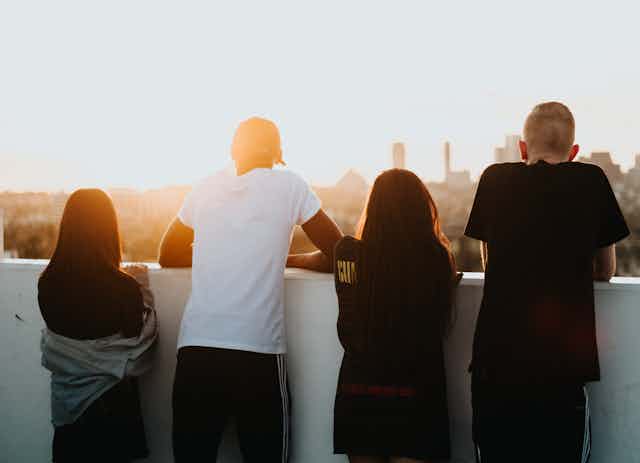Four young people viewed from behind as they look out over a city.