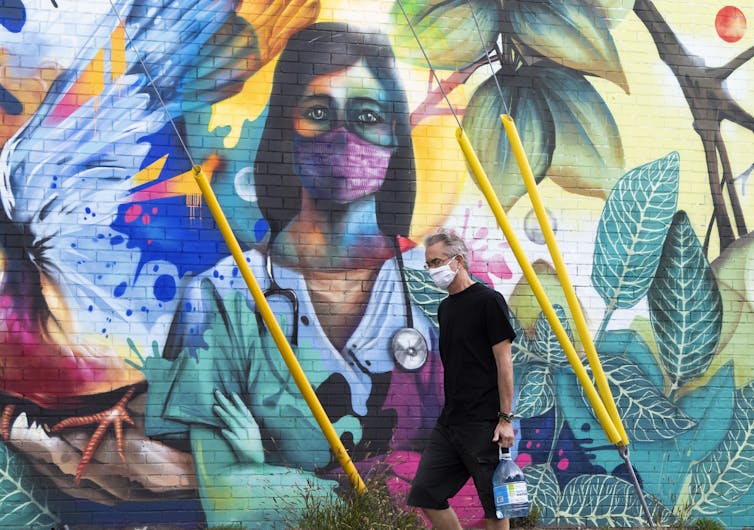 A man walks by a mural of a health-care worker in scrubs