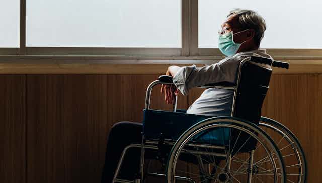 A man in a wheelchair and a mask on his own looking out of the window