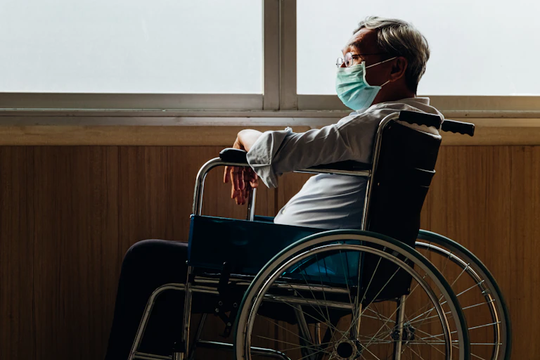 A man in a wheelchair and a mask on his own looking out of the window