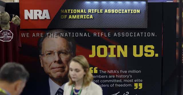 Woman stands next to an NRA poster.
