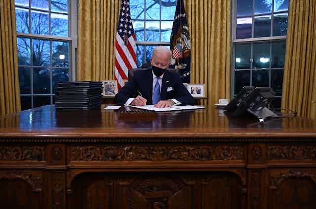 President Joe Biden signs a document in the Oval Office