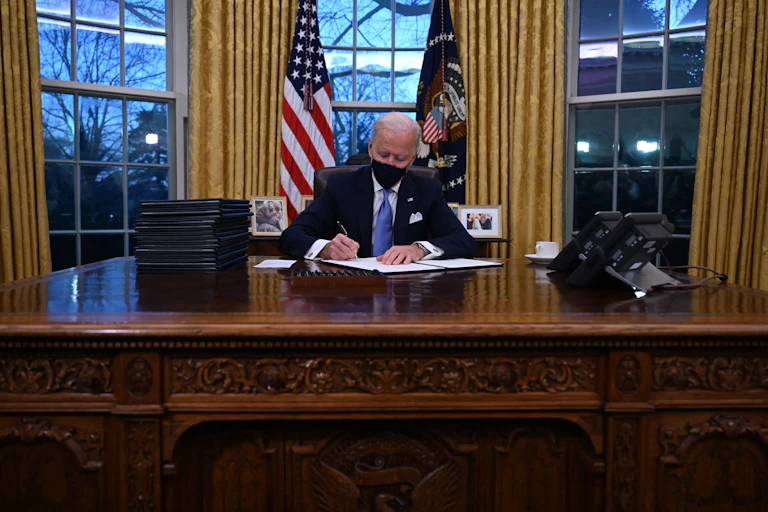 President Joe Biden signs a document in the Oval Office