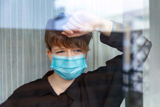 Teenager wearing face mask leans against window looking out