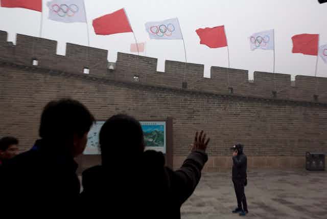 People look up at flags on a section of the Great Wall of China