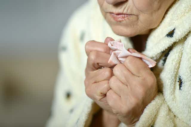 Cold, older woman clutching a handkerchief.