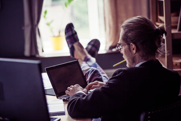 Man at home with laptop, suit and slippers on. Feet on desk.