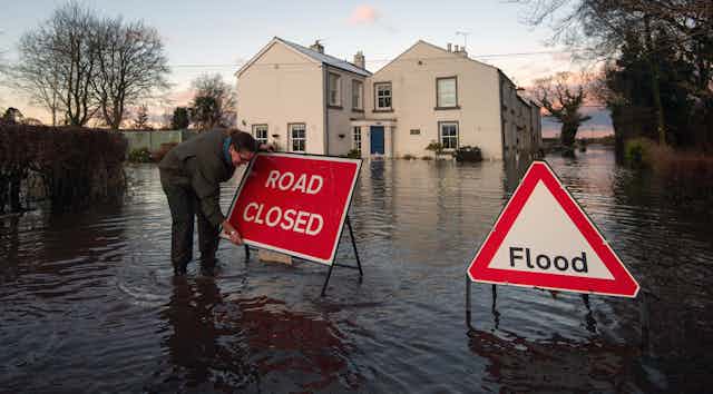 Woman putting 'road closed' sign up in flooded street.