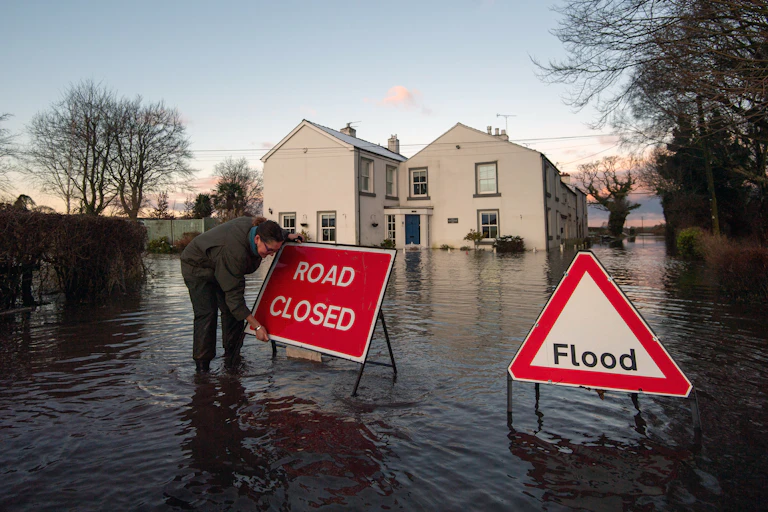 Woman putting 'road closed' sign up in flooded street.