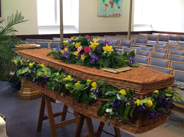 A wicker coffin decorated with beautiful flowers sitting in an empty church.