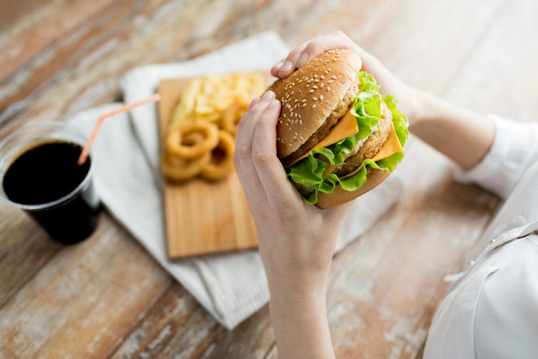 A person holding a hamburger, with soda and onion rings in the background.