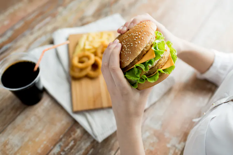 A person holding a hamburger, with soda and onion rings in the background.