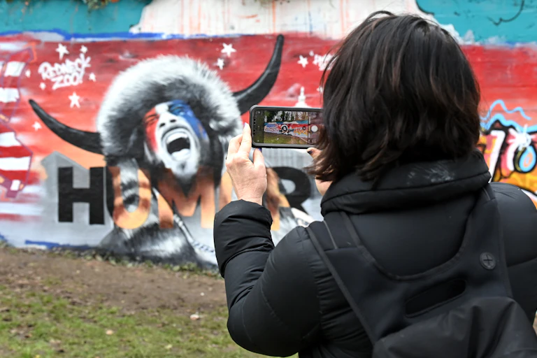 A woman photographs a mural depicting the 'QAnon Shaman.'