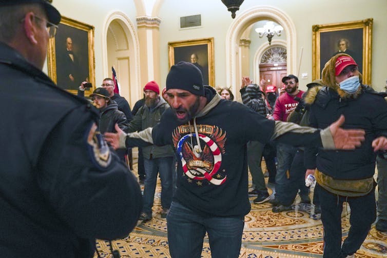 Jensen in a black hat and black t-shirt leads a mob of riotors.