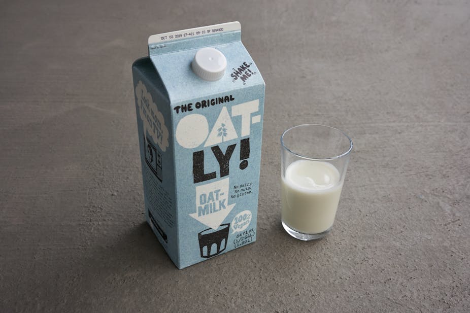 A carton of Oatly beside a glass of oat milk