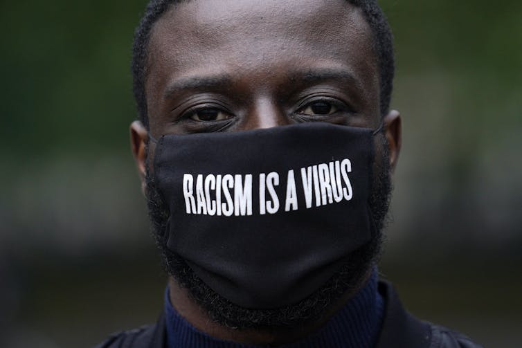 A man wears a black mask that says 'Racism is a virus'