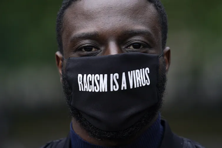 A man wears a black mask that says 'Racism is a virus'