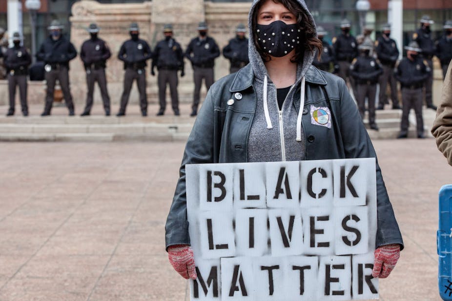 A woman holds a sign of black lives matter in front of a row of Ohio state troopers
