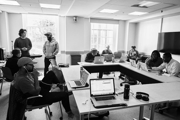 A group of students sit on desks while using their laptops in a classroom.